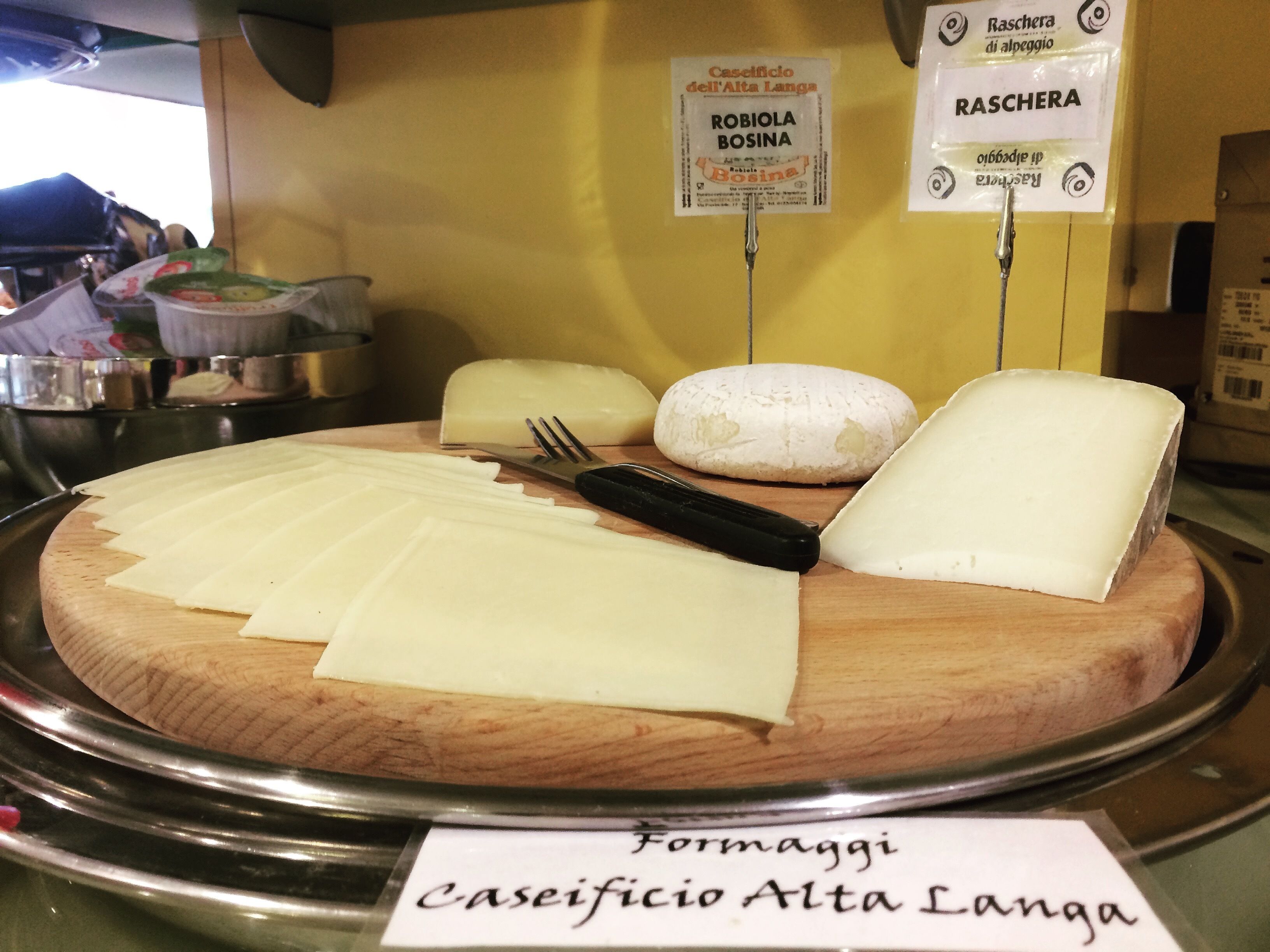 Una tabla de quesos con distintos tipos de queso, un cuchillo y un tenedor sobre una tabla de madera.