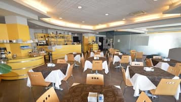 A hotel dining area with round tables, chairs, and a buffet counter.