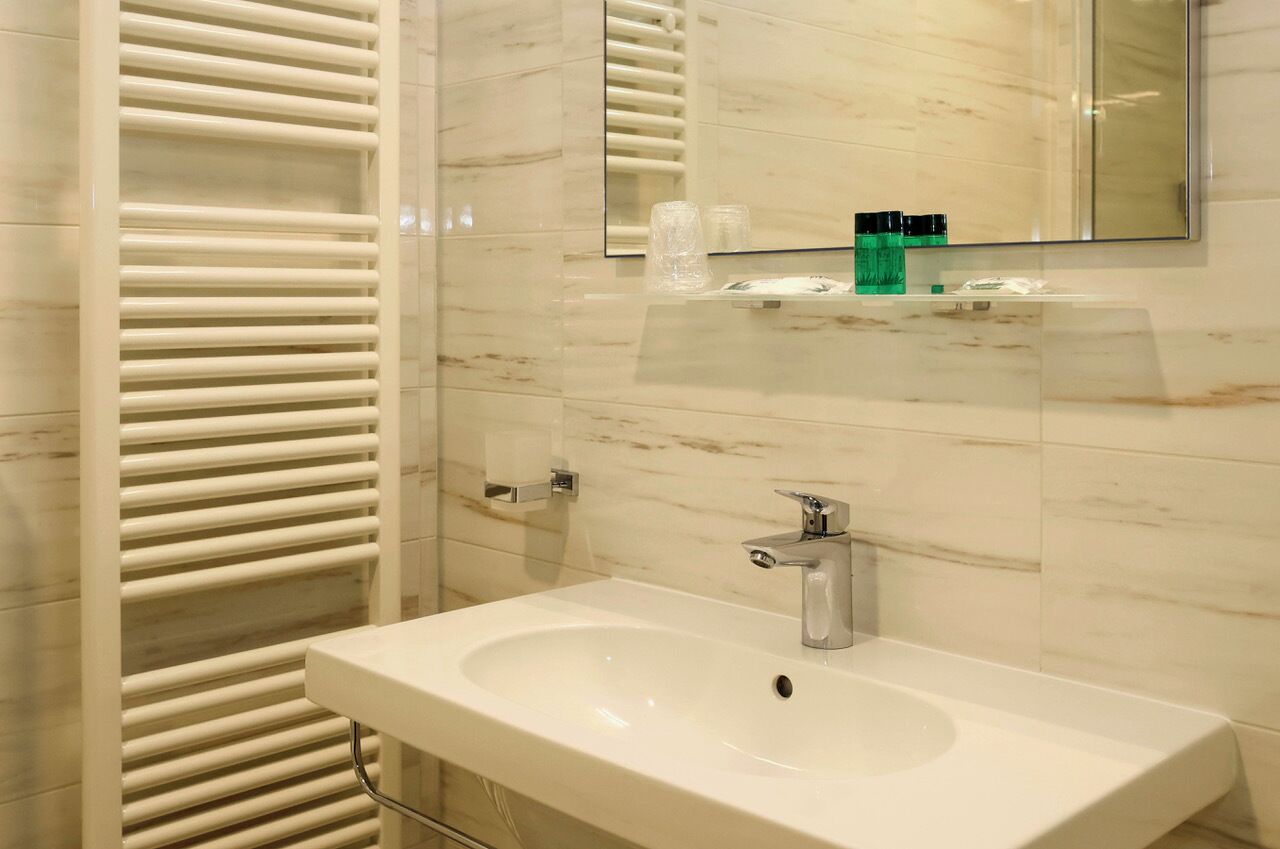Un baño moderno con un lavamanos blanco, un espejo y un perchero para toallas.