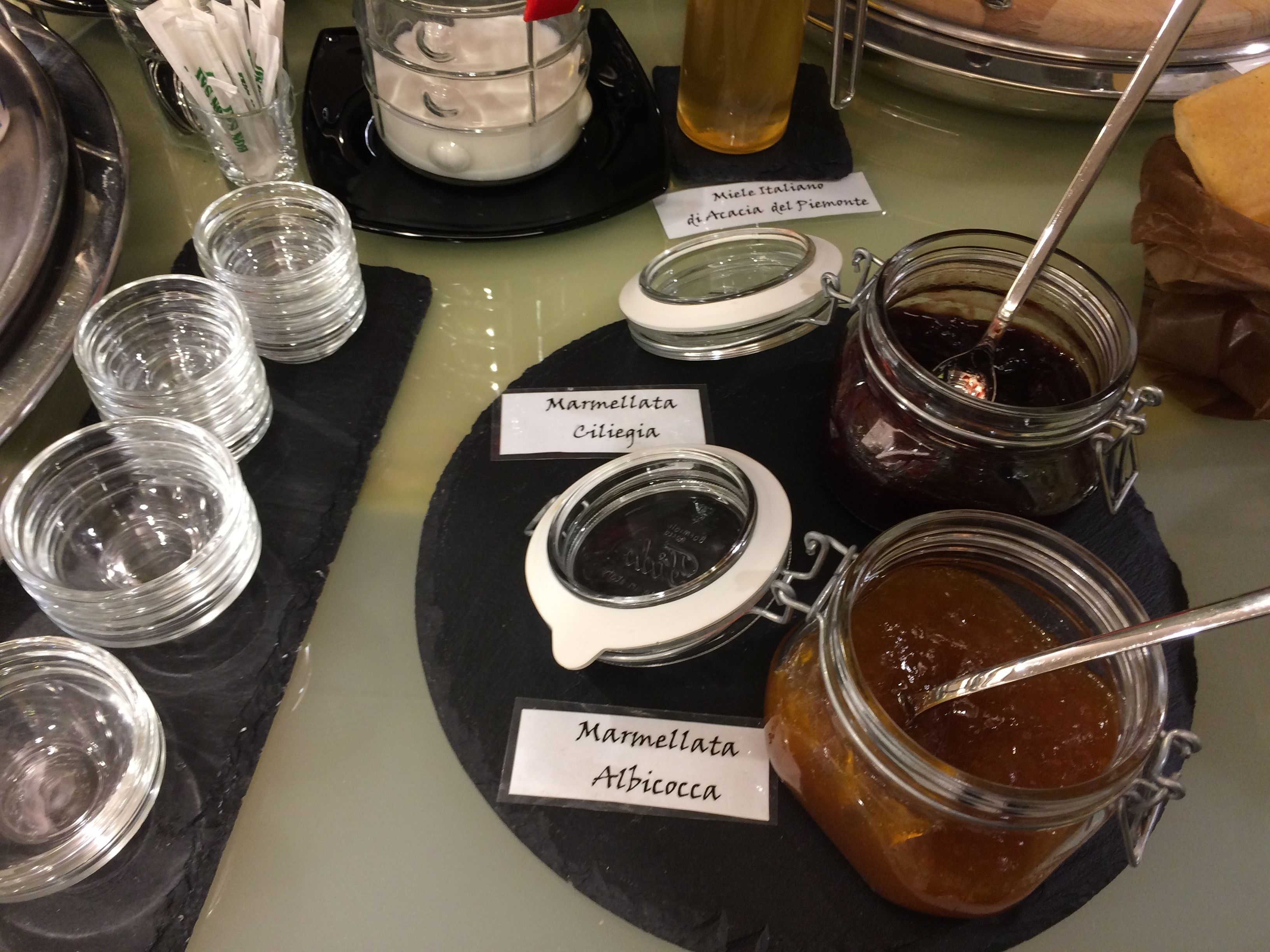 A buffet table with various jars of marmellata, including 'Marmellata Ciliegia' and 'Marmellata Alicocca'.