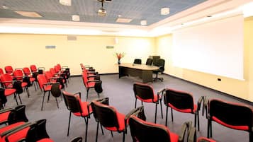 A conference room with rows of red chairs, a large table, and a projector on the ceiling.