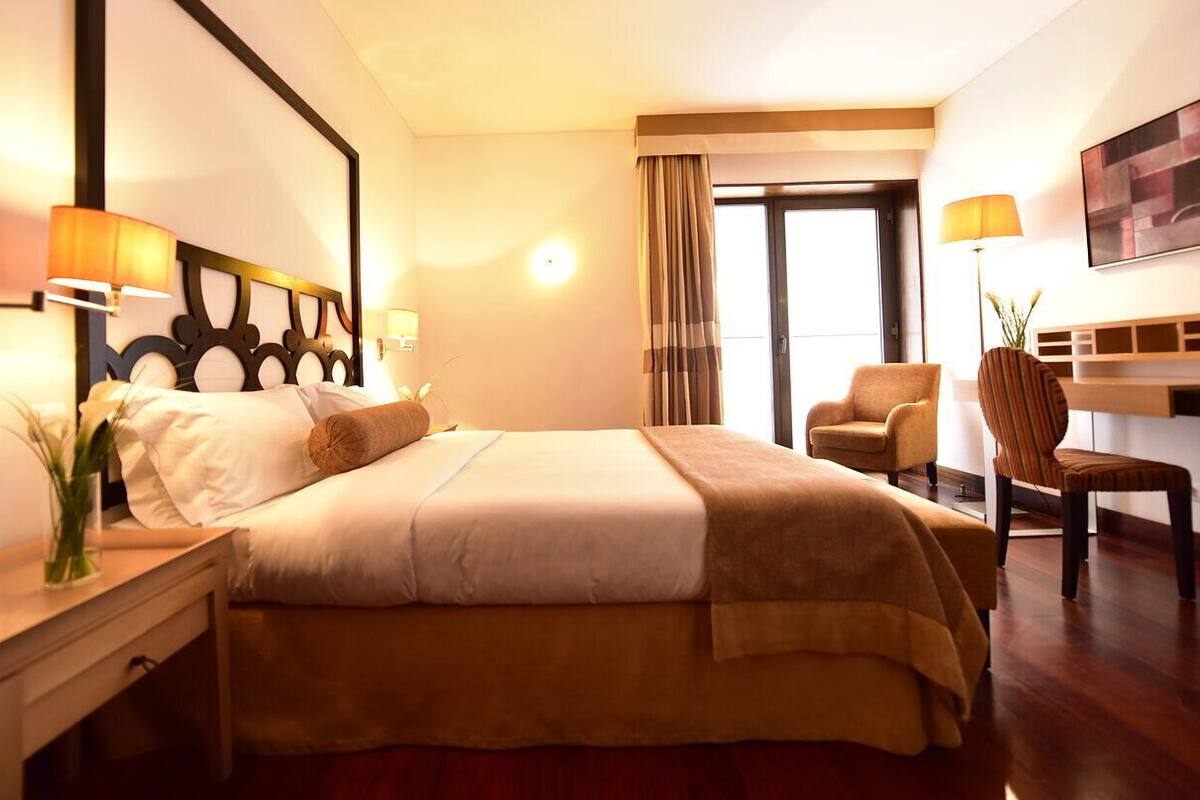 A hotel room with a bed, a desk, two chairs, and a large window.