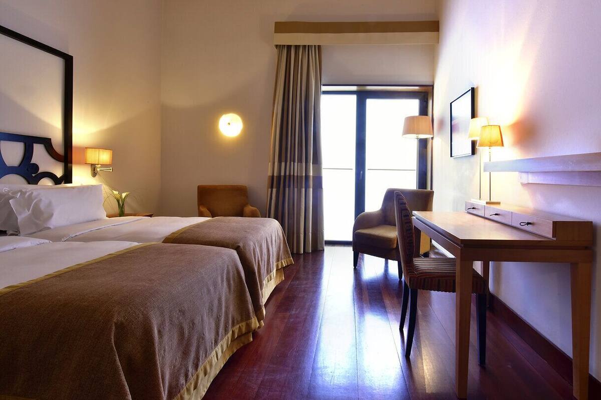A hotel room with two beds, a desk, a chair, and a large window.