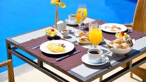 A breakfast table by a pool with a variety of foods and drinks.