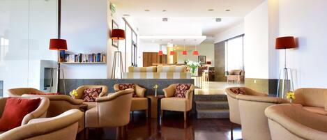 Un moderno vestíbulo de hotel con sofás color beige, una mesa de centro a cuadros y lámparas rojas.