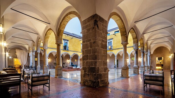 An interior courtyard with stone columns, arches, and seating areas.