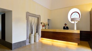 A reception desk with a wooden counter and a large circular window. There are vases with branches on the wall beside the desk.