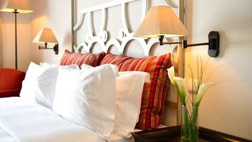 Una cama bien tendida con almohadillas rojas y blancas a rayas, una mesita de noche con un florero y lámparas fijadas a la pared.