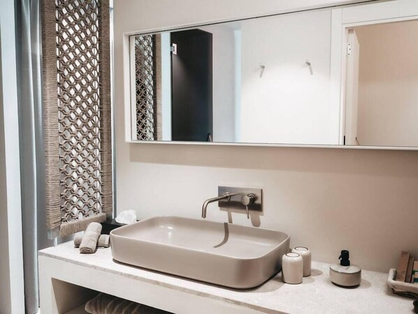 A modern bathroom with a rectangular sink, a mirror above it, and a towel rack with folded towels. - Hotel Llum Portocolom (Felanitx)