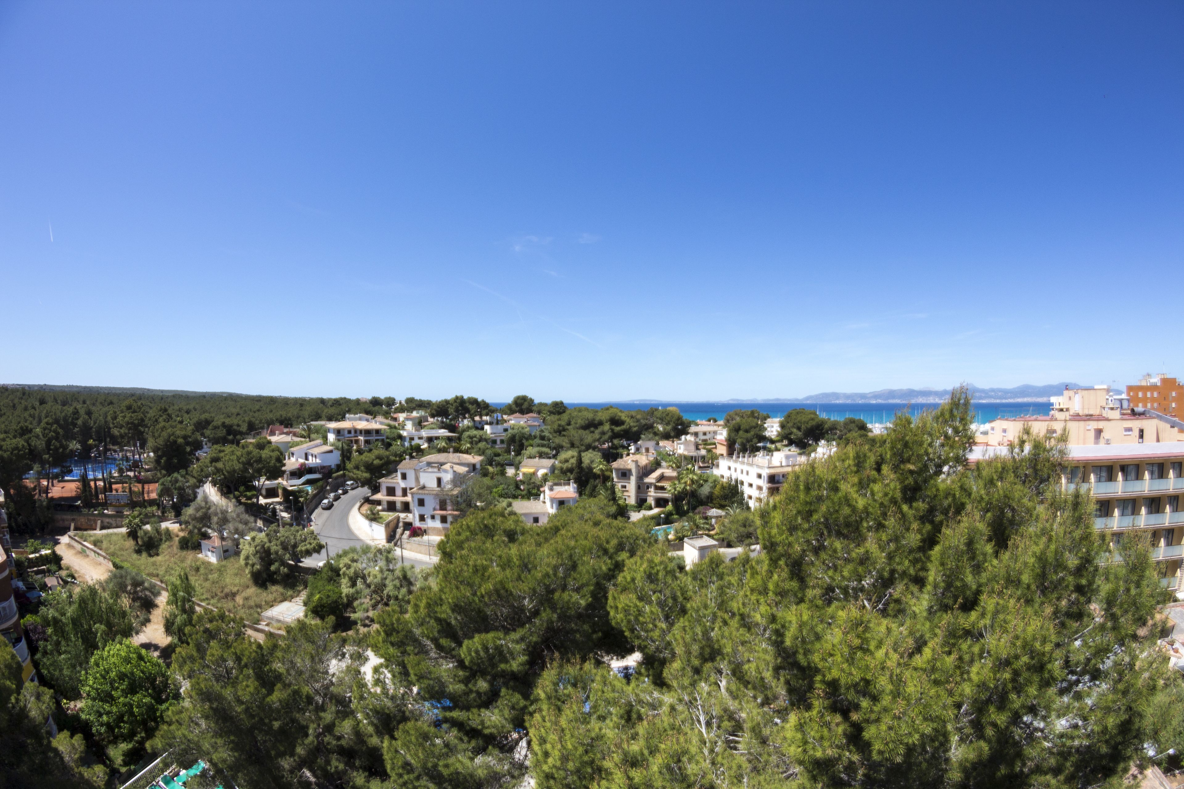 A coastal town with residential buildings, a clear blue sky, and a view of the sea.