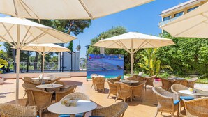 An outdoor patio area with wicker furniture, large umbrellas, and a large screen displaying a sports event. - Hotel JS Paradise Sport - Adults Only (Llucmajor)