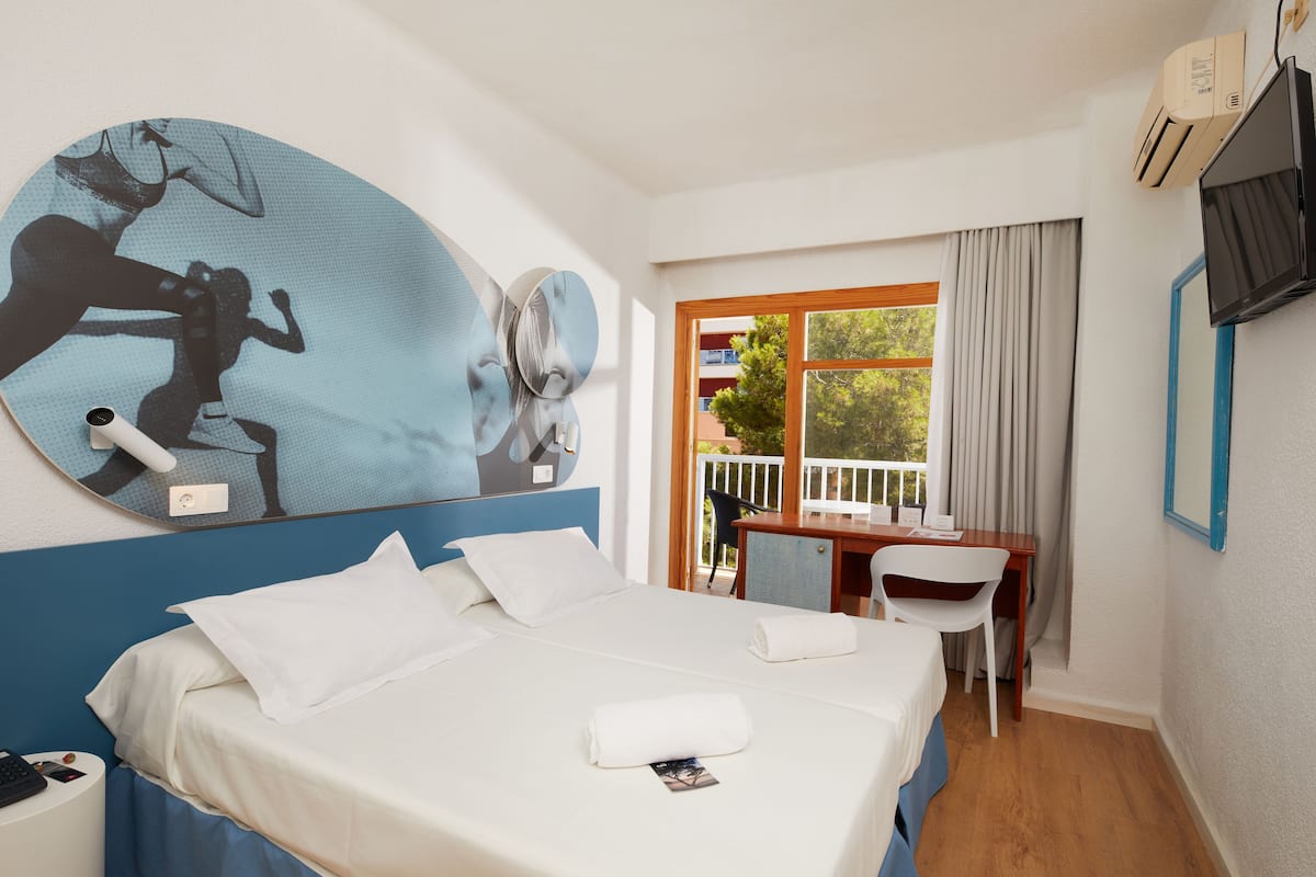 Ein Hotelzimmer mit Bett, Schreibtisch, Stuhl, Fernseher und einem großen Fenster mit Vorhängen.