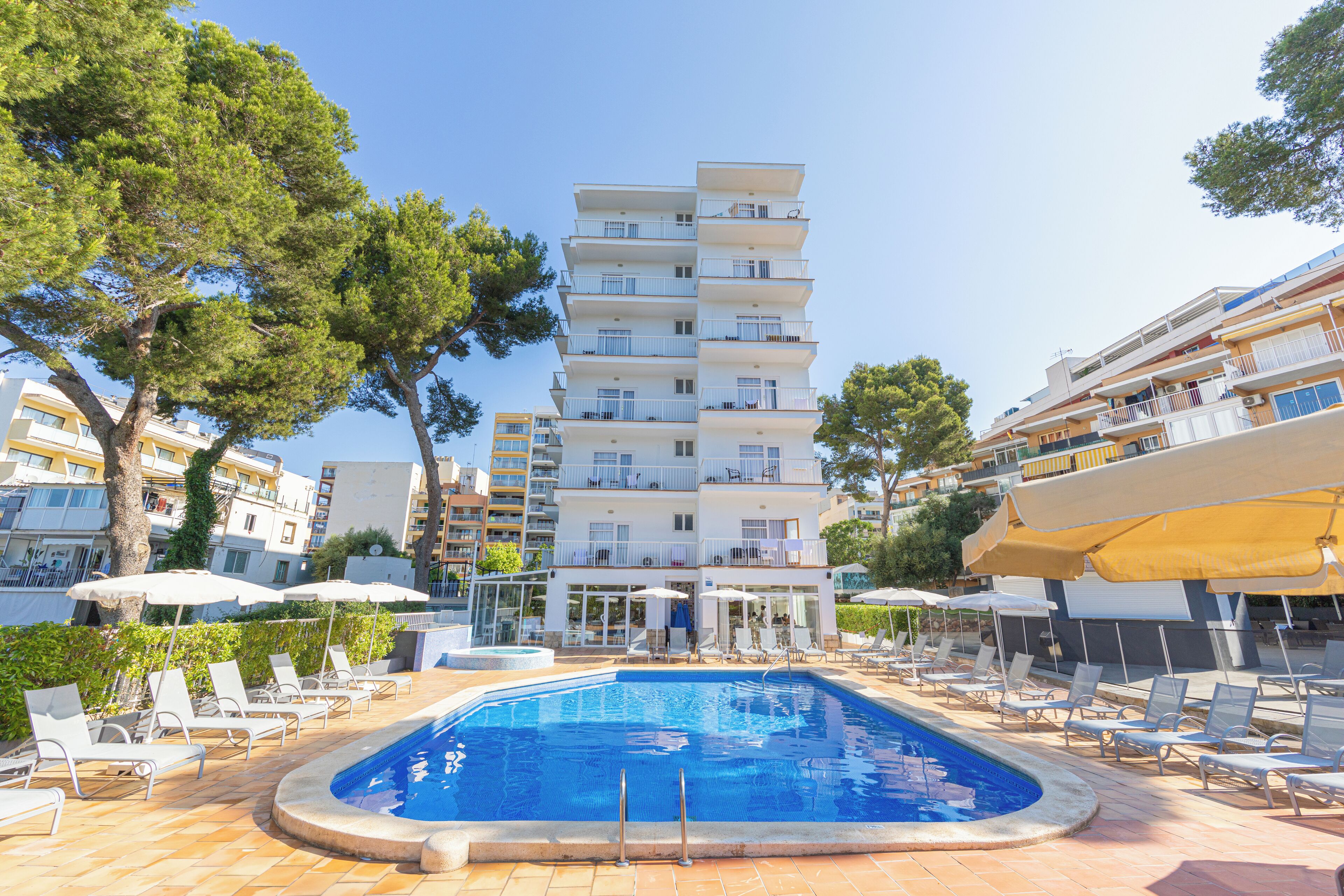 A swimming pool with lounge chairs and umbrellas, surrounded by multi-story buildings.