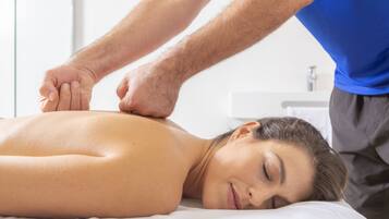 A person receiving a massage on a bed in a room with a white wall and a small window.