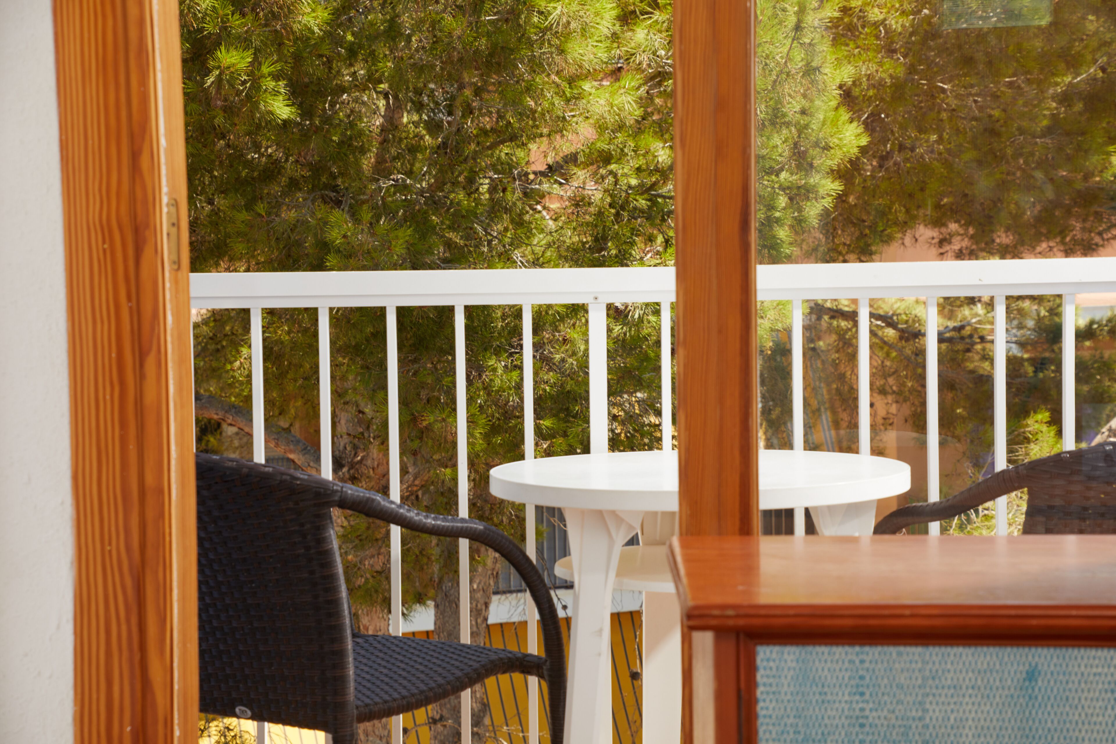 A balcony with a white table and chairs, surrounded by a white railing, overlooking a forested area.