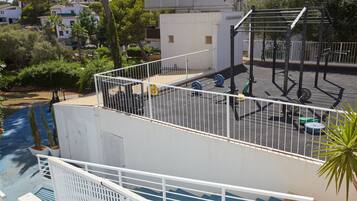 Un gimnasio en la azotea con equipo de ejercicios, una piscina y vistas de edificios y árboles circundantes.