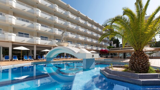 Een zwembadgedeelte van een hotel met een helderblauw zwembad, ligbedden en een palmboom.