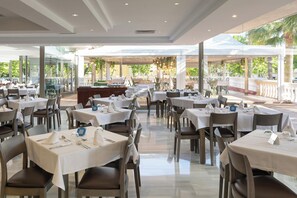 Un restaurante con varias mesas, sillas y un separador de vidrio.