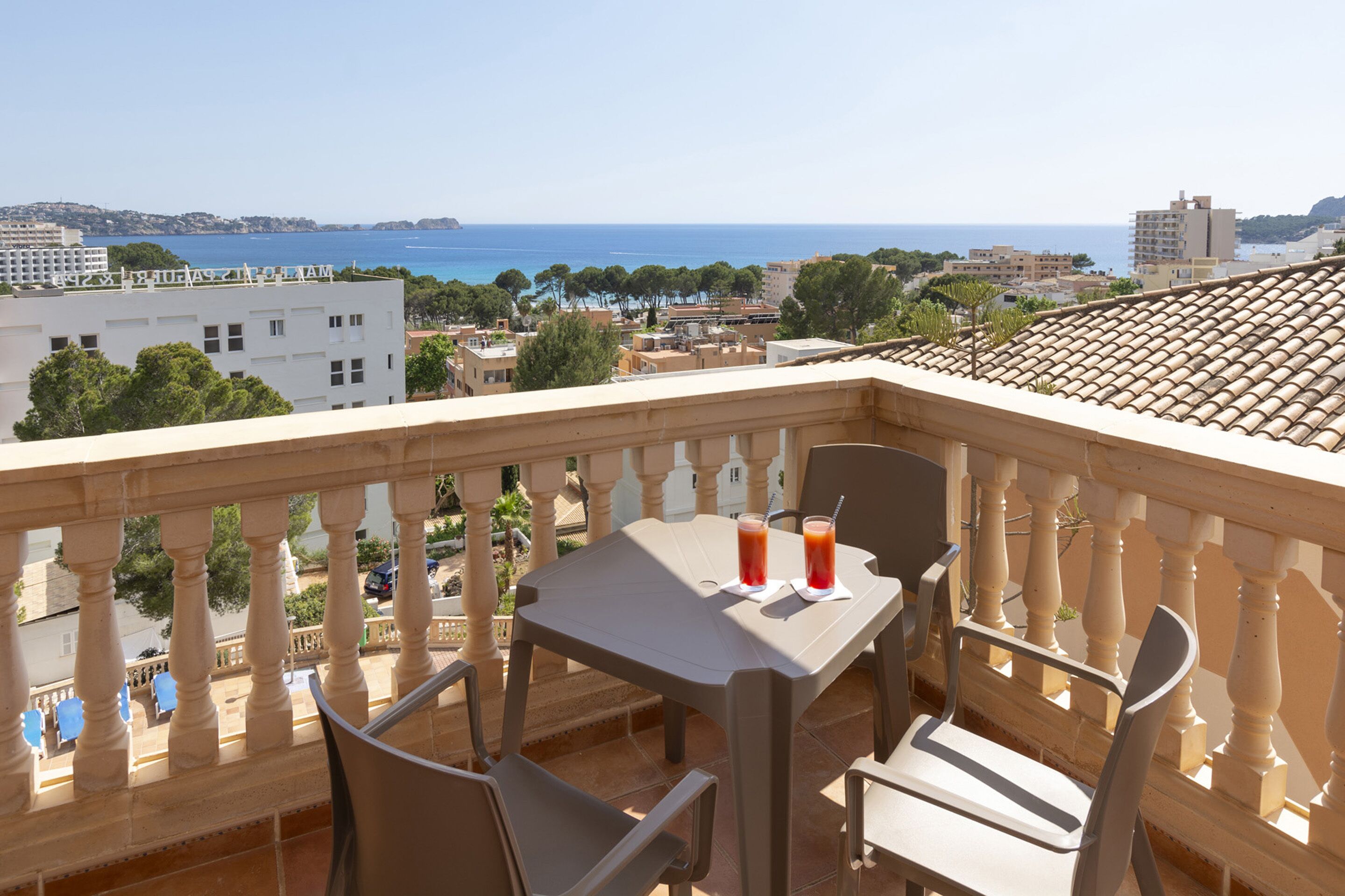 A balcony with a table and chairs, overlooking a coastal cityscape with buildings and the sea.