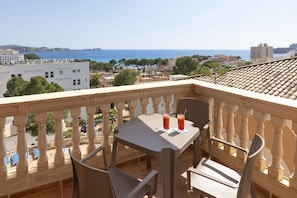 Un balcón con mesa y sillas, con vista a un paisaje urbano costero con edificios y el mar.
