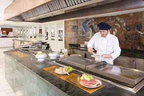 Un chef prepara comida en una barra, rodeado de diversos ingredientes y utensilios de cocina.
