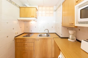 Una cocina compacta con armarios de madera, un lavamanos de acero inoxidable, un microondas y una cafetera.