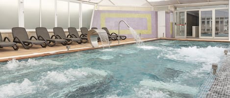 En swimmingpool med et vandfald, liggestole og et overdækket område med glasdøre.