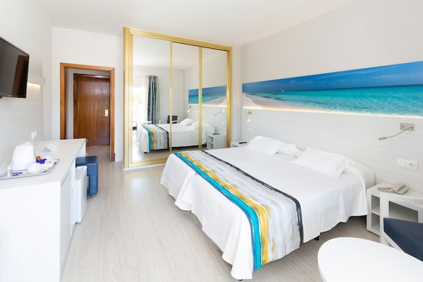 Habitación de hotel con una cama grande, un escritorio, una silla, un espejo y un cuadro de una playa.