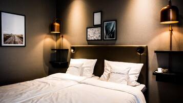 A hotel room with a large bed, two bedside tables, a headboard, and wall-mounted lamps.