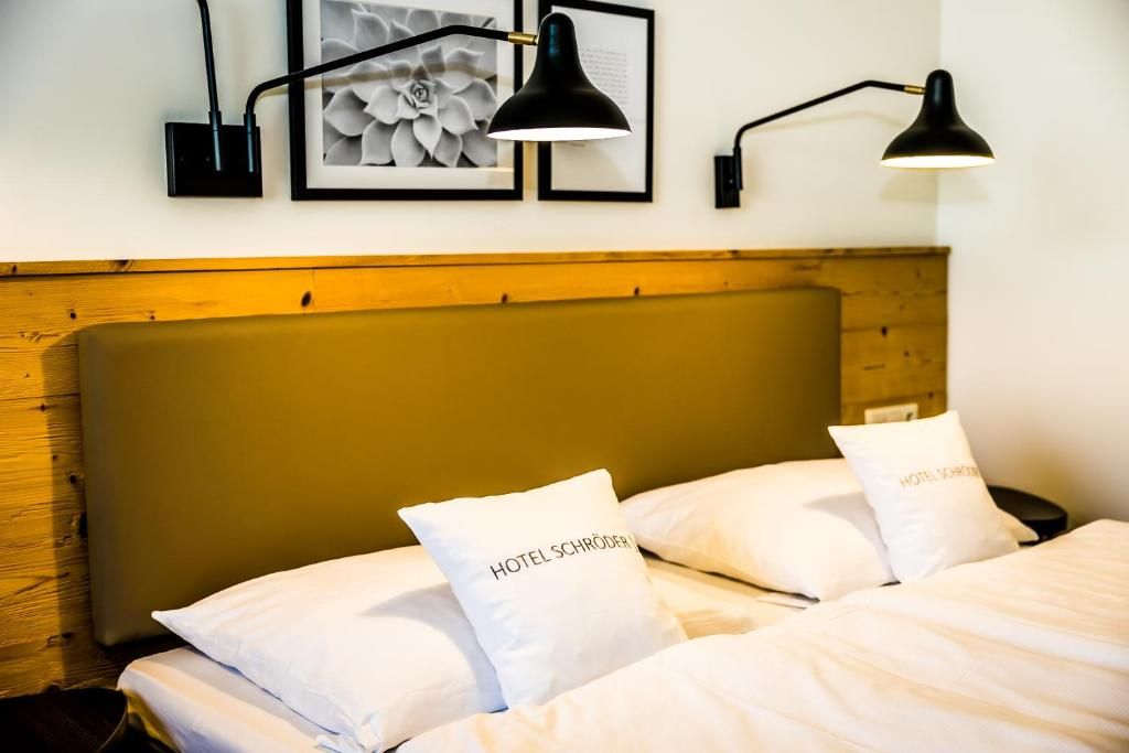 Una habitación de hotel con cabecera de madera, cama con ropa blanca y dos lámparas de pared negras.