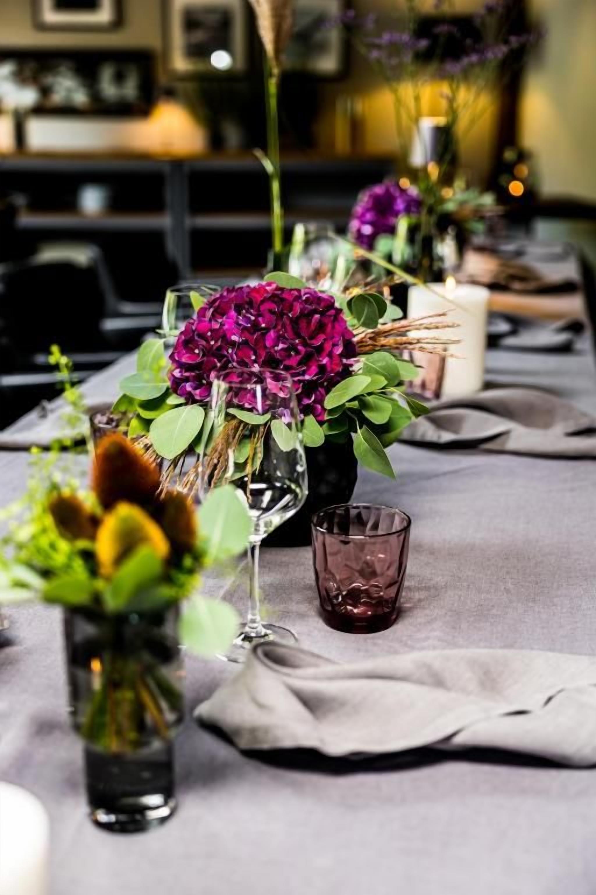 Una mesa dispuesta con jarrones de flores, vasos y una servilleta de tela.