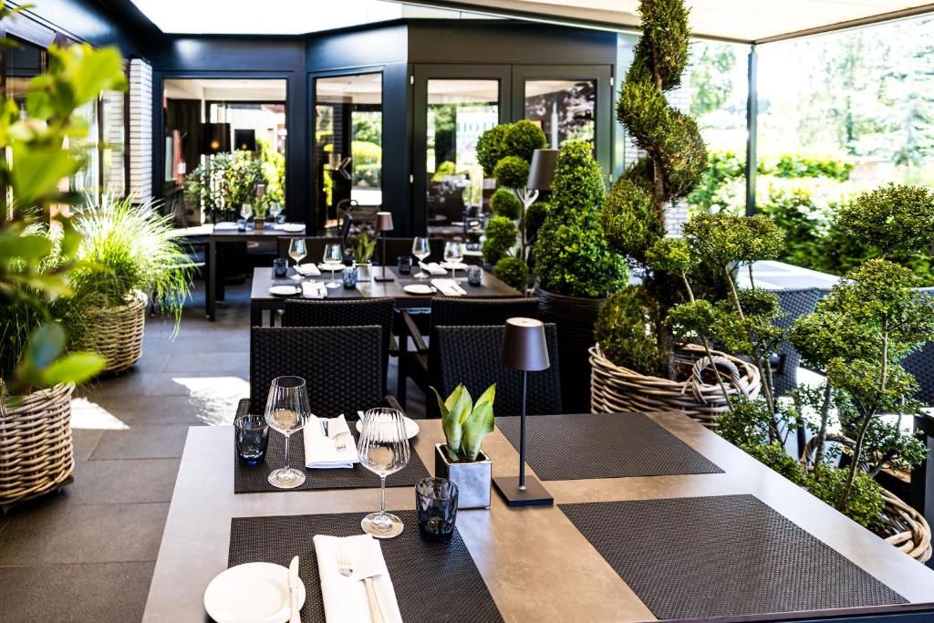 An outdoor dining area with tables set for two, surrounded by greenery and potted plants.