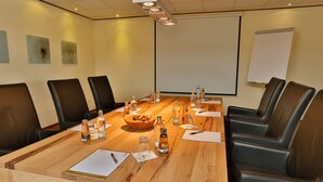 A conference room with a long wooden table, black leather chairs, and a projector screen. - Schröder Hotel and Restaurant (Gross Meckelsen)