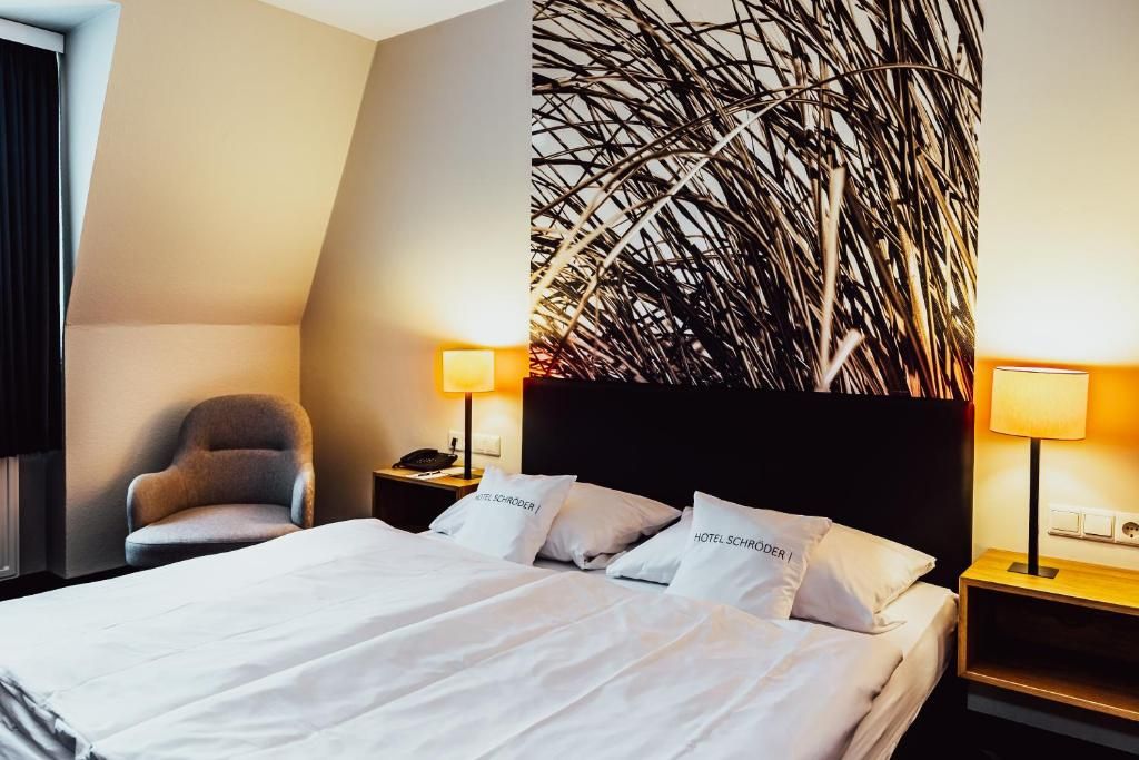 A hotel room with a bed, two bedside tables, a chair, and a decorative wall with a plant.