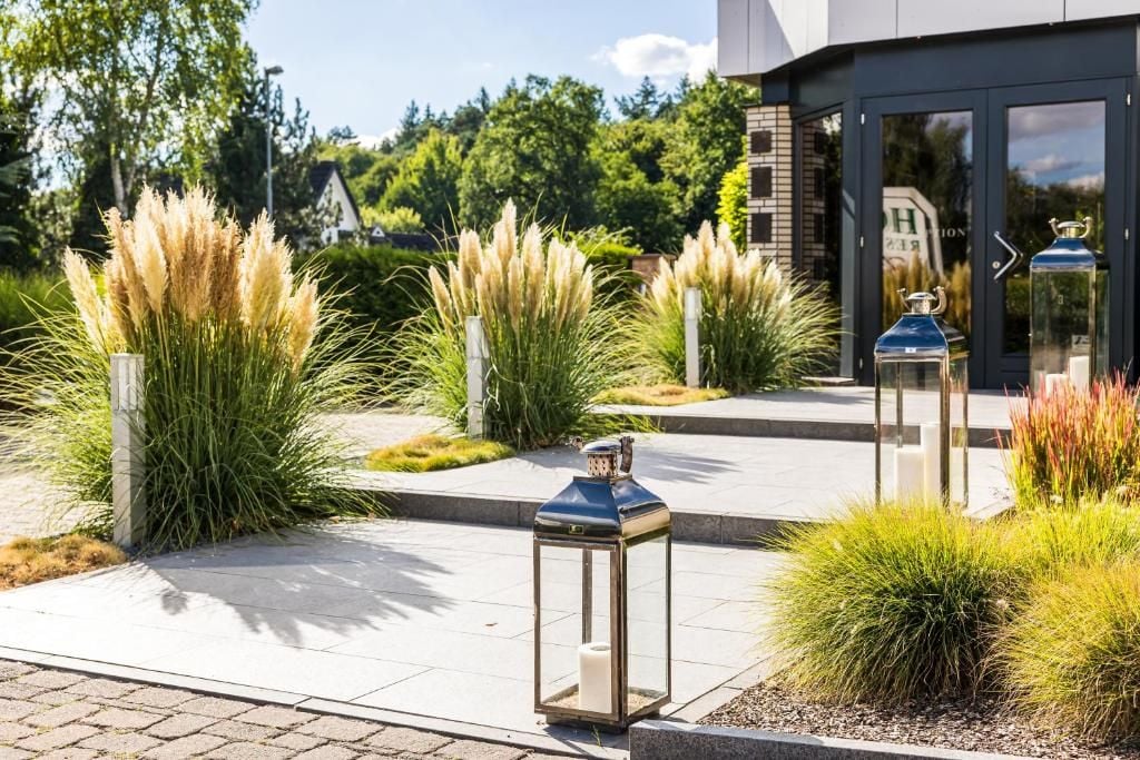 A modern building with a glass entrance, outdoor lanterns, and ornamental grasses.