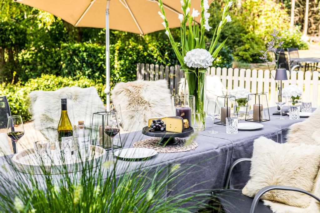 Een terras met een eettafel gedekt voor twee personen, met een wijnfles, glazen, een kaasplankje en een vaas met bloemen.