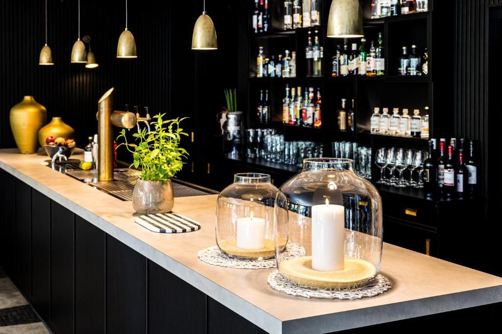 A bar area with a long counter, decorative glass jars, a potted plant, and a shelf of liquor bottles.