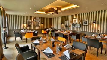 A hotel dining area with striped wallpaper, multiple tables set for dining, and modern pendant lighting.