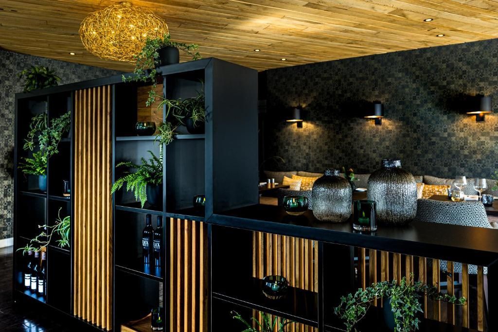 Un interior moderno con techo de madera, estanterías negras con plantas y jarrones decorativos.