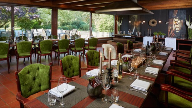 A restaurant with wooden tables and chairs, candles, and a view of greenery outside. - Schröder Hotel and Restaurant (Gross Meckelsen)