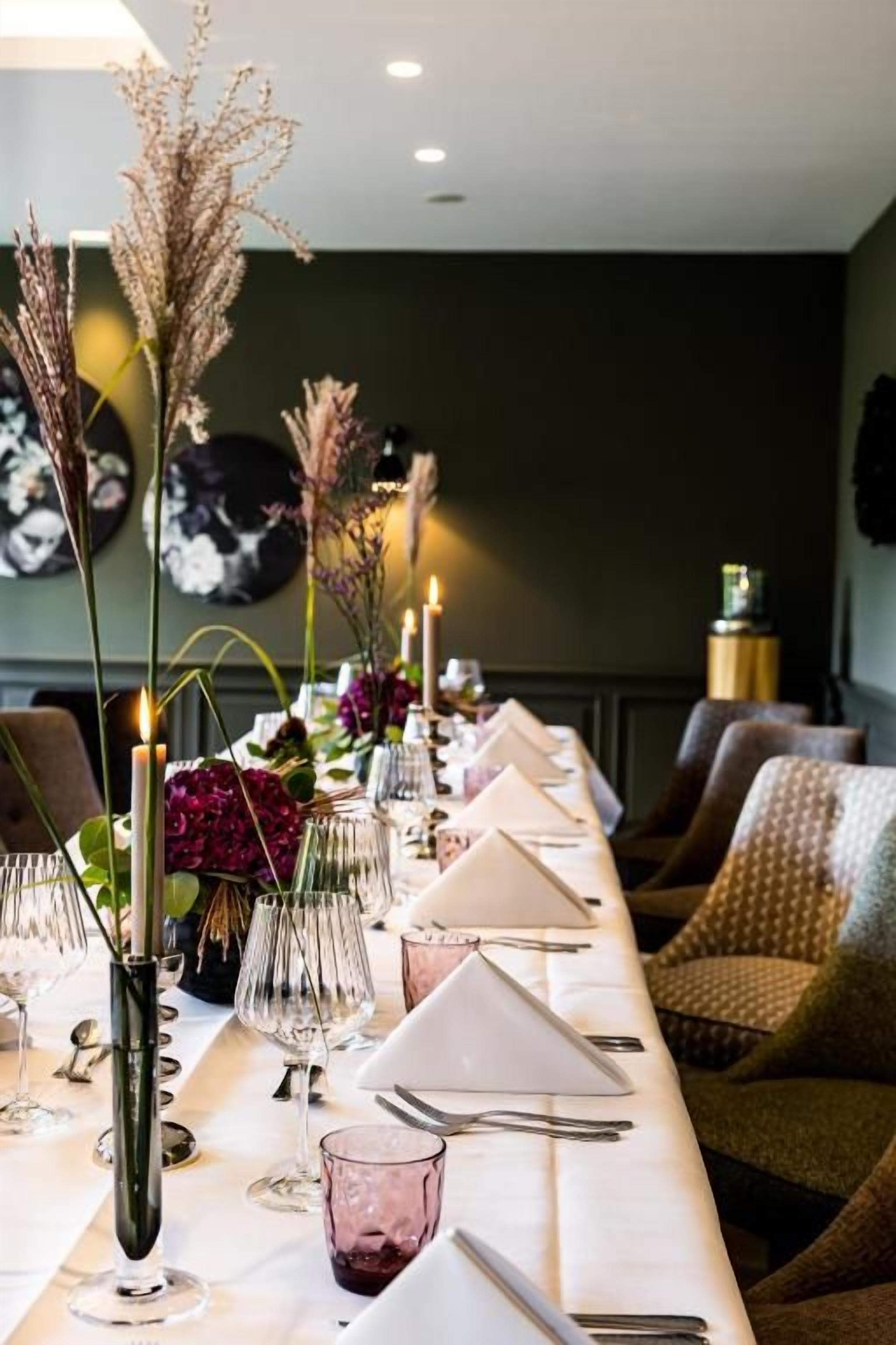 A dining table set with glassware, candles, and floral arrangements.