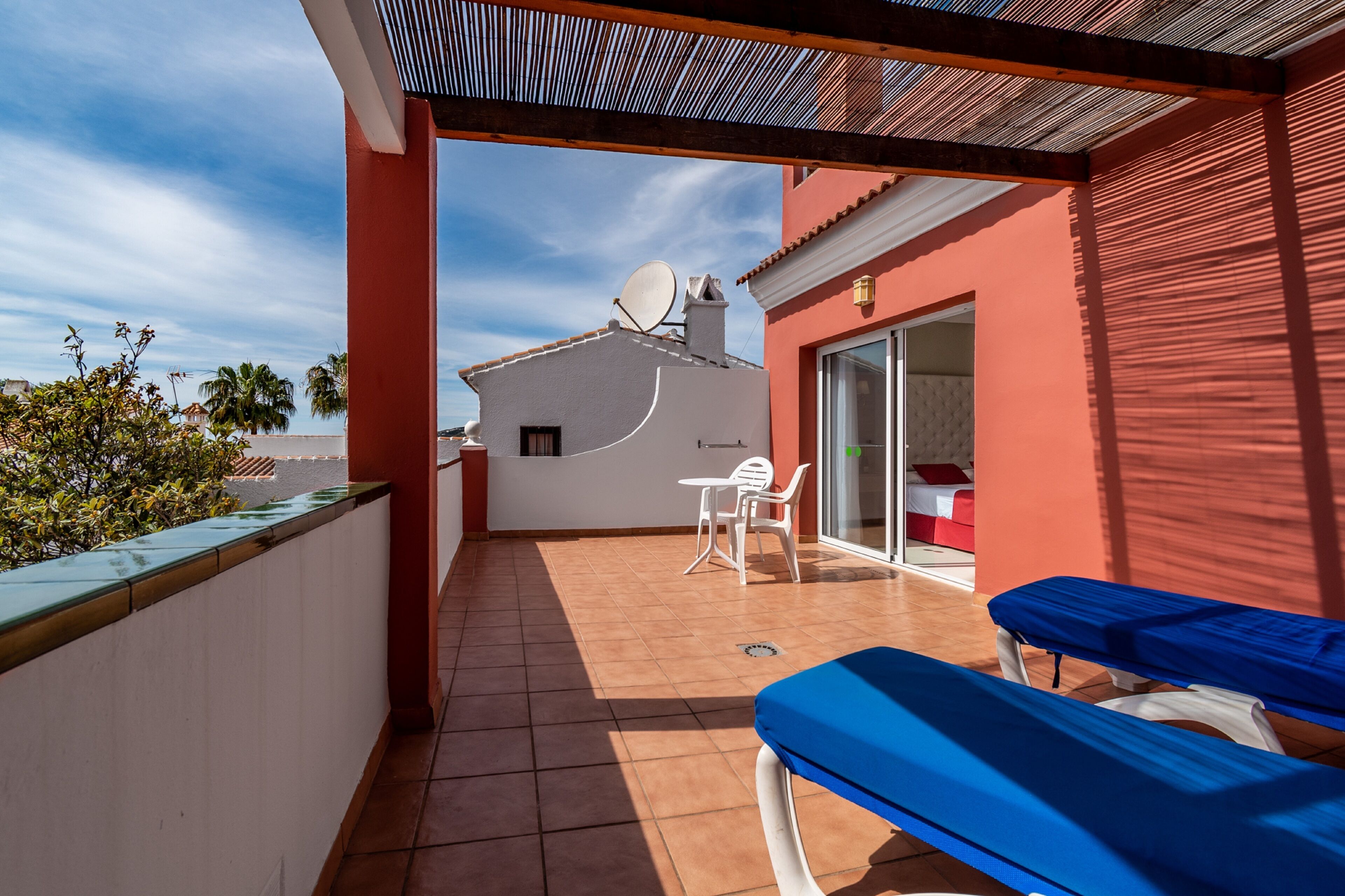 Ein Balkon mit zwei blauen Lounge-Stühlen, einem weißen Tisch und einer Glastür, die zu einem Innenraum führt.