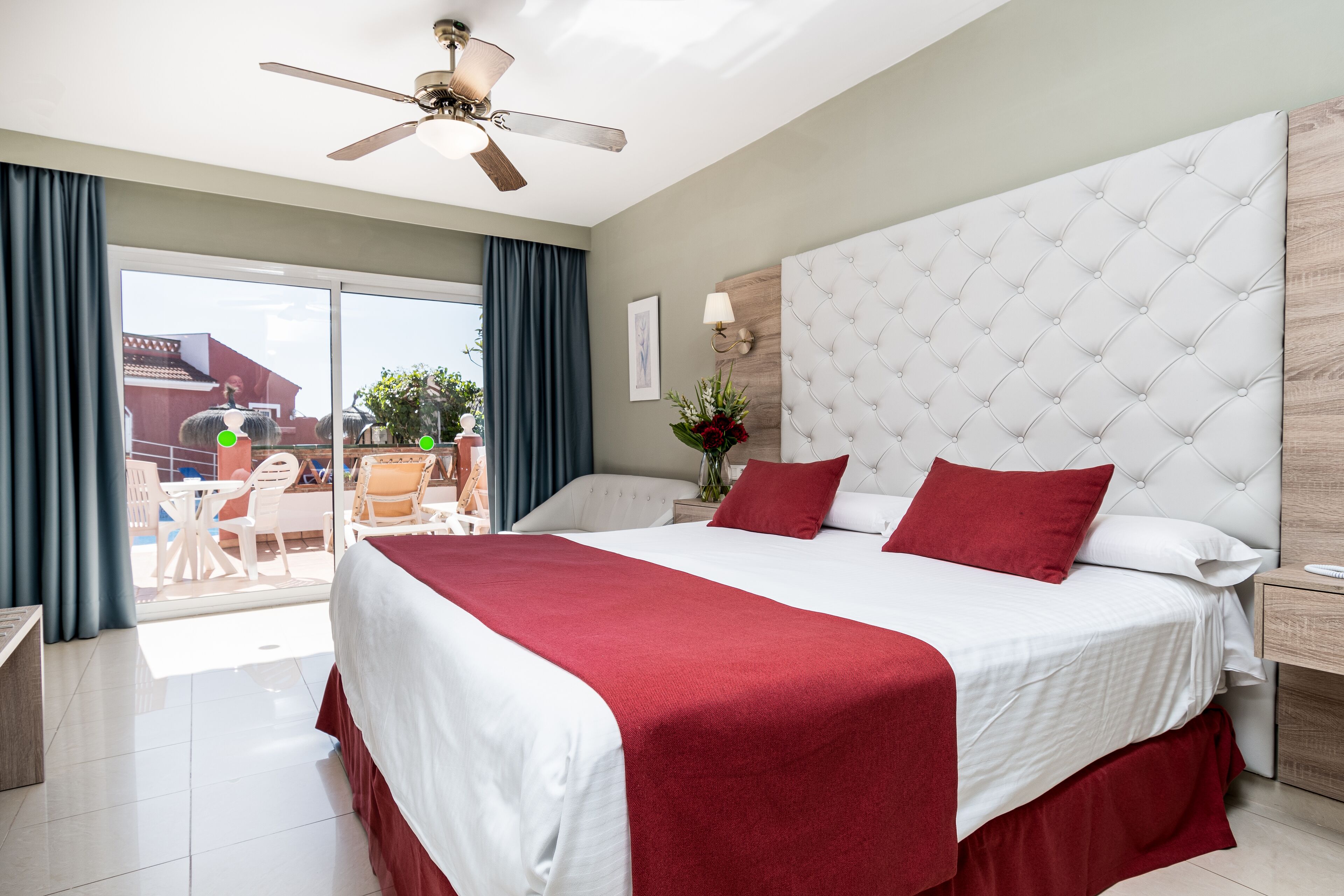 Une chambre d’hôtel avec un grand lit, un ventilateur de plafond, un balcon avec des meubles d’extérieur et une vue sur l’extérieur.