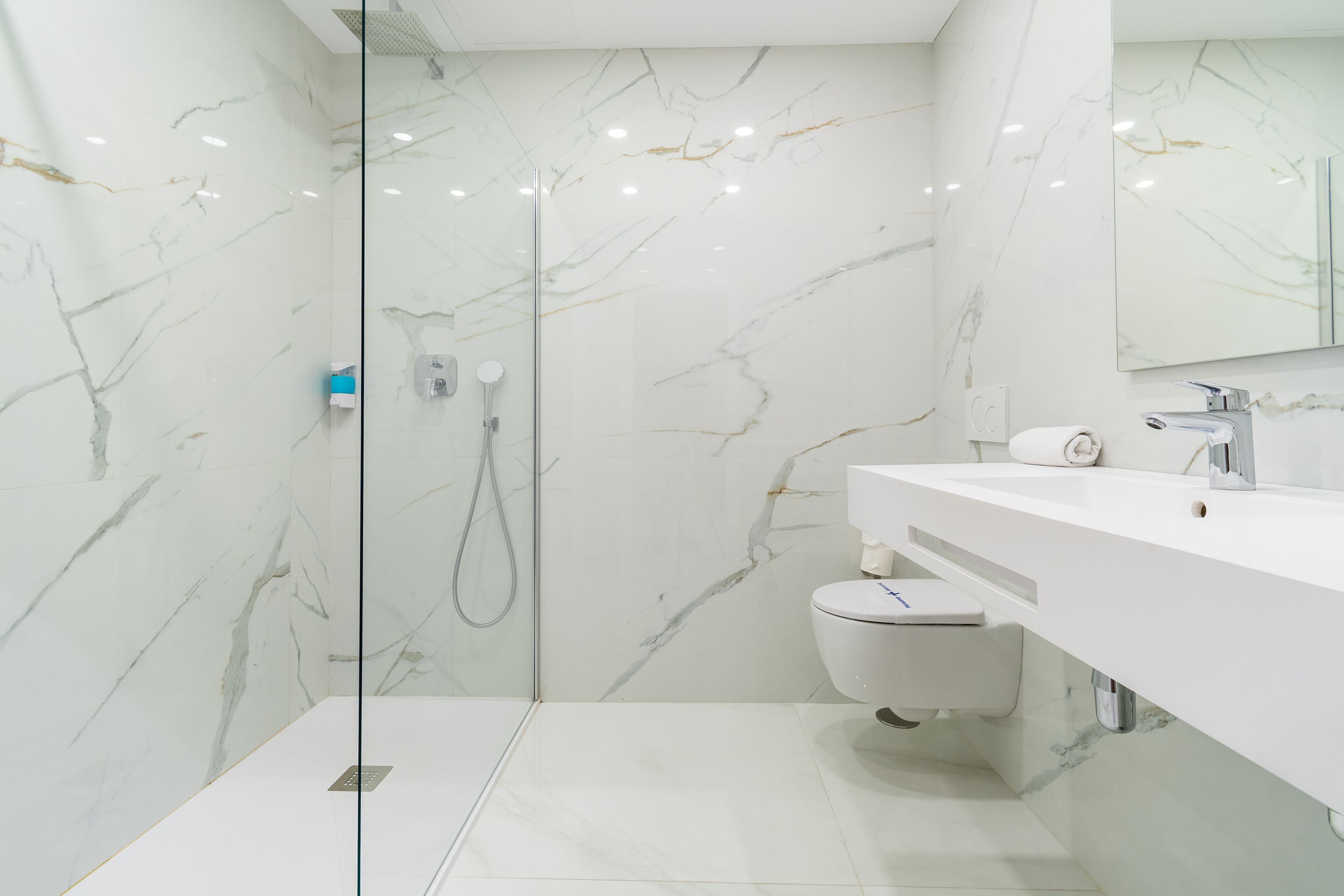 A modern bathroom with a glass-enclosed shower, white marble walls, and a white sink with a mirror above.
