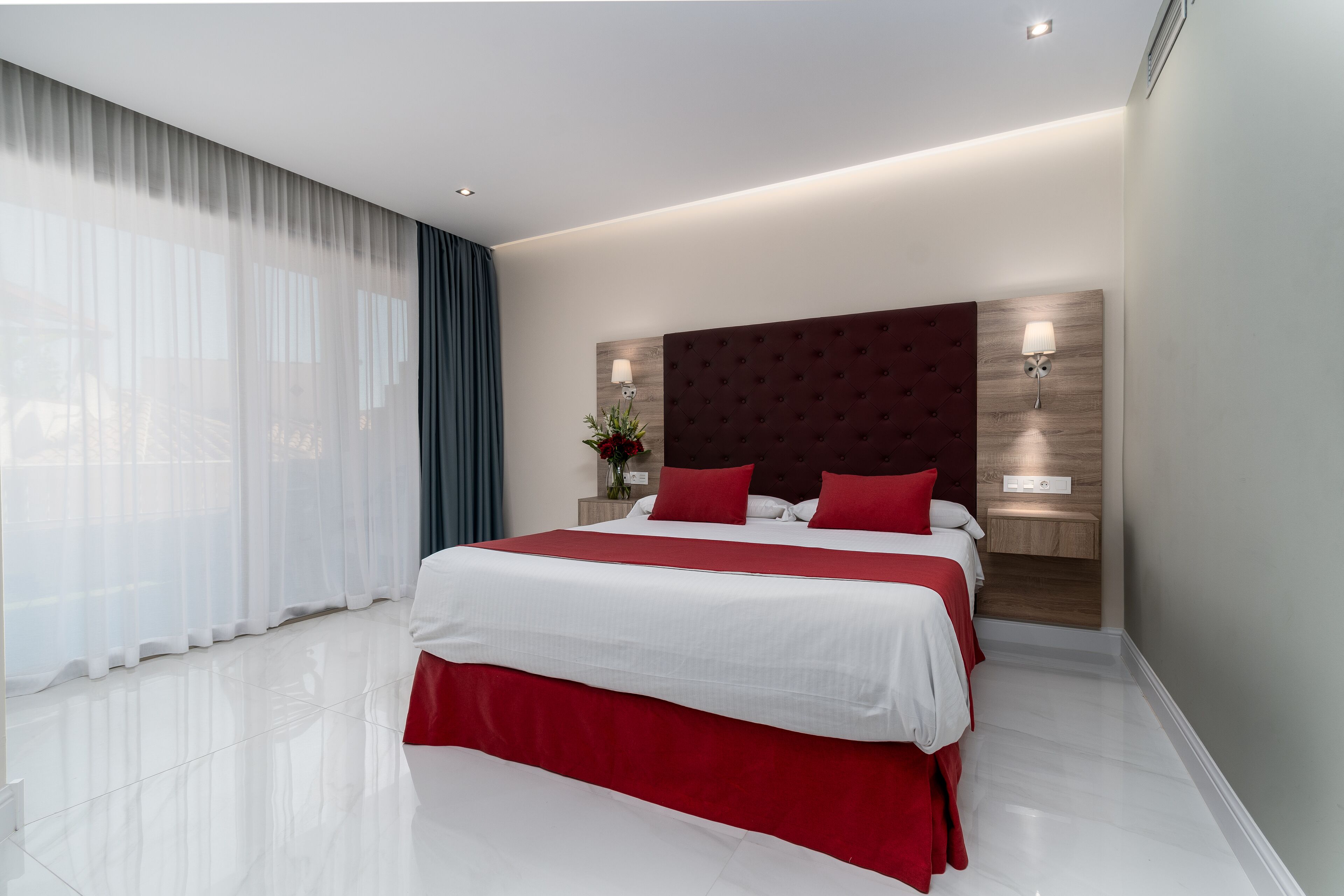 A modern hotel bedroom with a large bed, a wooden headboard, and a nightstand with a lamp.