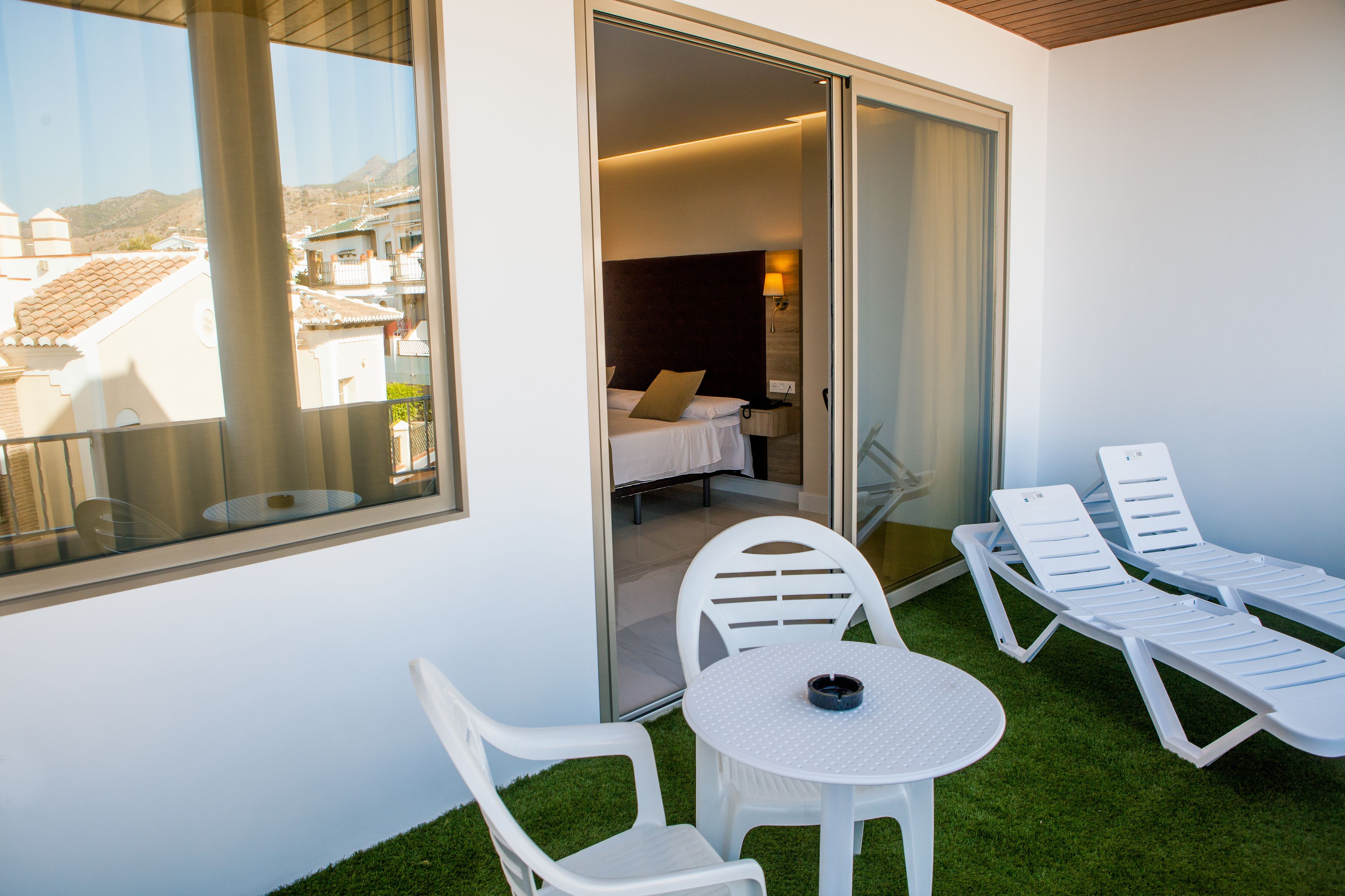 Uma varanda com vista para edifícios, uma cama e uma mesa com cadeiras.