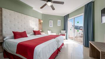 Habitación de hotel con una cama grande, ventilador de techo, balcón con vistas y una mesita de noche de madera.