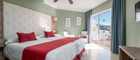 A hotel room with a large bed, a ceiling fan, a balcony with a view, and a wooden side table.
