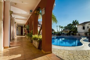 A hotel corridor with a pool area, including a swimming pool, lounge chairs, and palm trees. - Hotel Los Arcos (Nerja)
