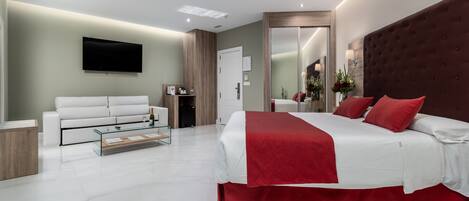 Una habitación de hotel moderna con una cama grande, un televisor de pantalla plana, un sofá y una mesa de centro de vidrio.